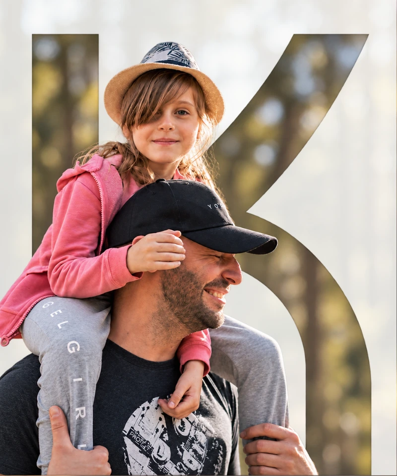 A father carrying his daughter on his shoulders, smiling outdoors